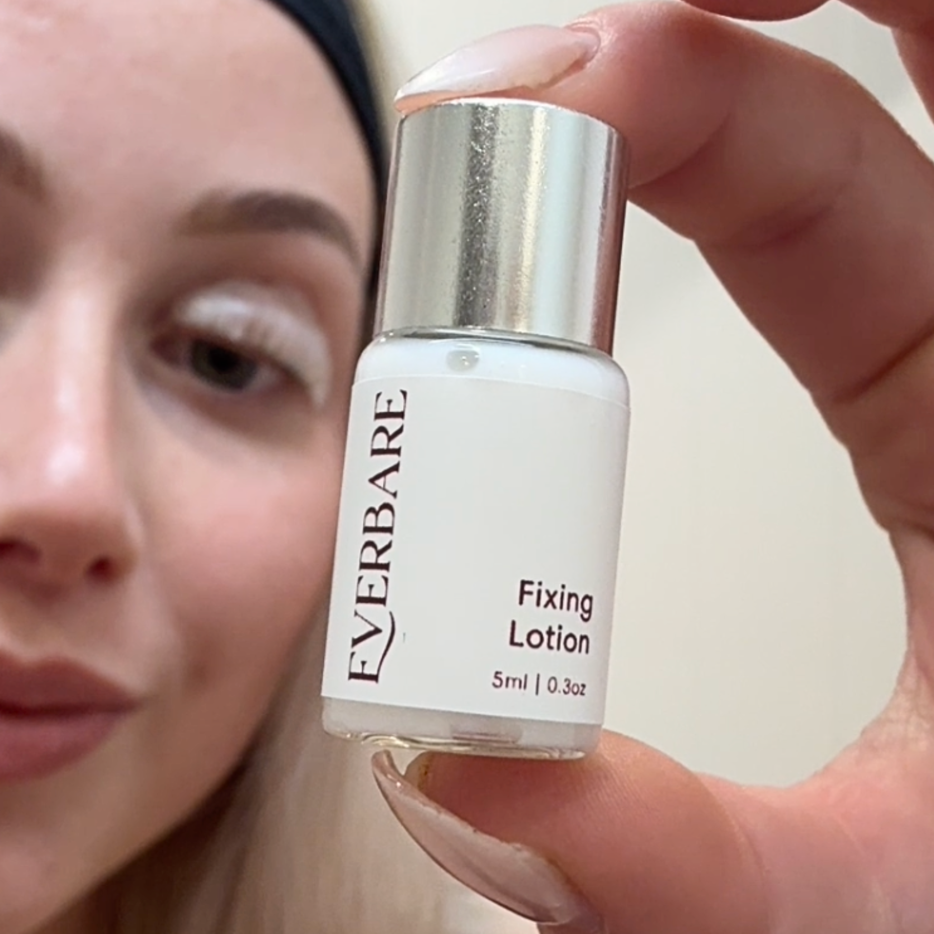 Person holding a bottle of Everbare Fixing Lotion close to their face.