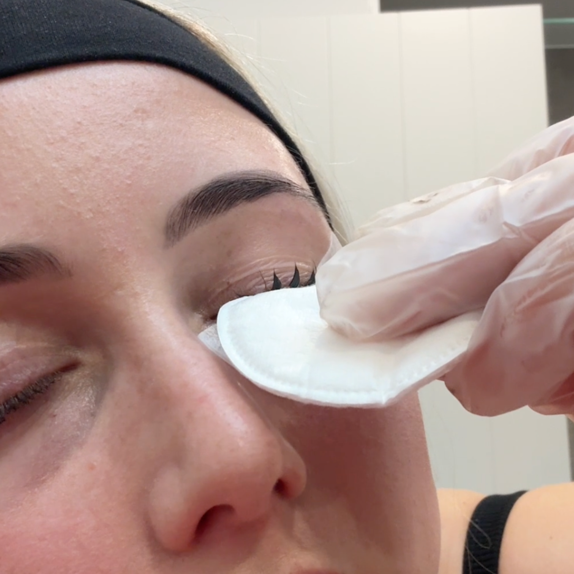 Person removing tint from eyelashes using a cotton pad