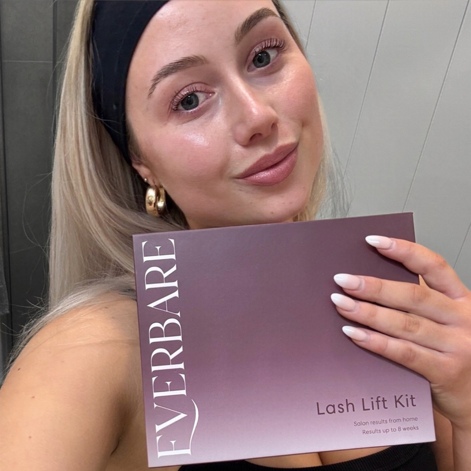 Woman holding a 'EVERBARE Lash Lift Kit' box in front of her face.